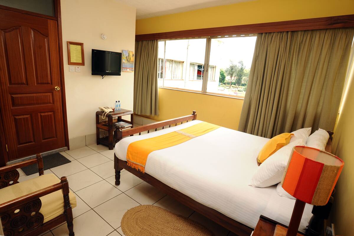 Habitación de hotel con cama, escritorio con teléfono, televisor en la pared y ventana con cortinas.