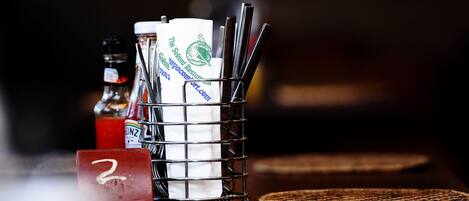 A metal container holding napkins and utensils, a bottle of ketchup, and a number "2" placard on a wooden table.