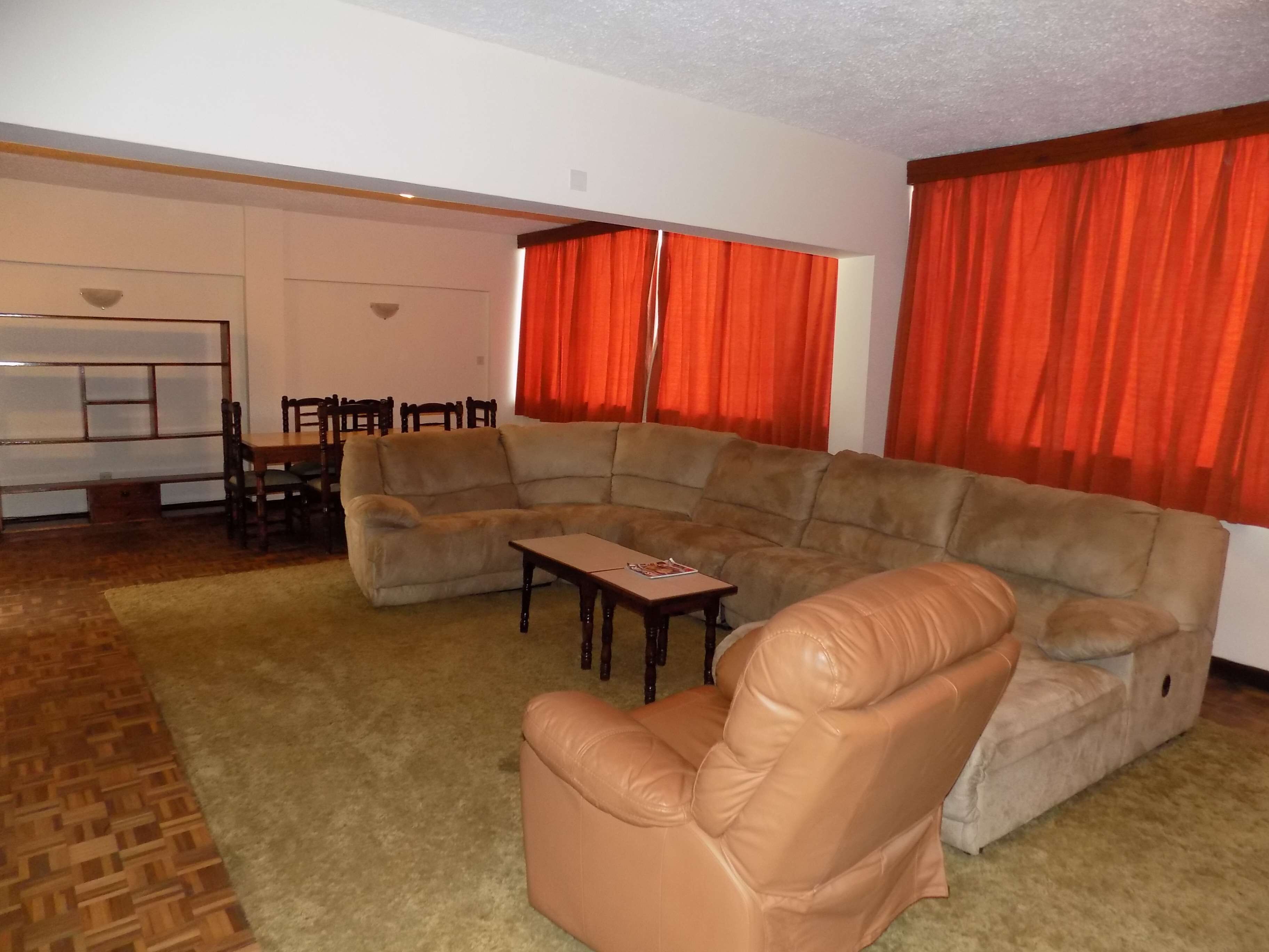 Una sala de estar con sofá modular, un sillón de cuero, una mesa de centro y un comedor con sillas y una mesa.