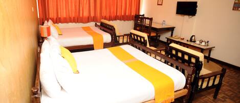 A hotel room with two beds, a wooden desk, a chair, a television, and a window with orange curtains.