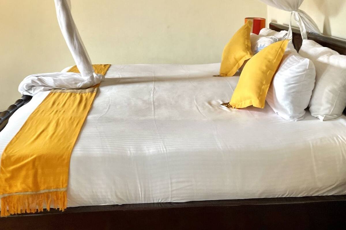 Una cama con dosel, ropa de cama blanca y almohadas amarillas.