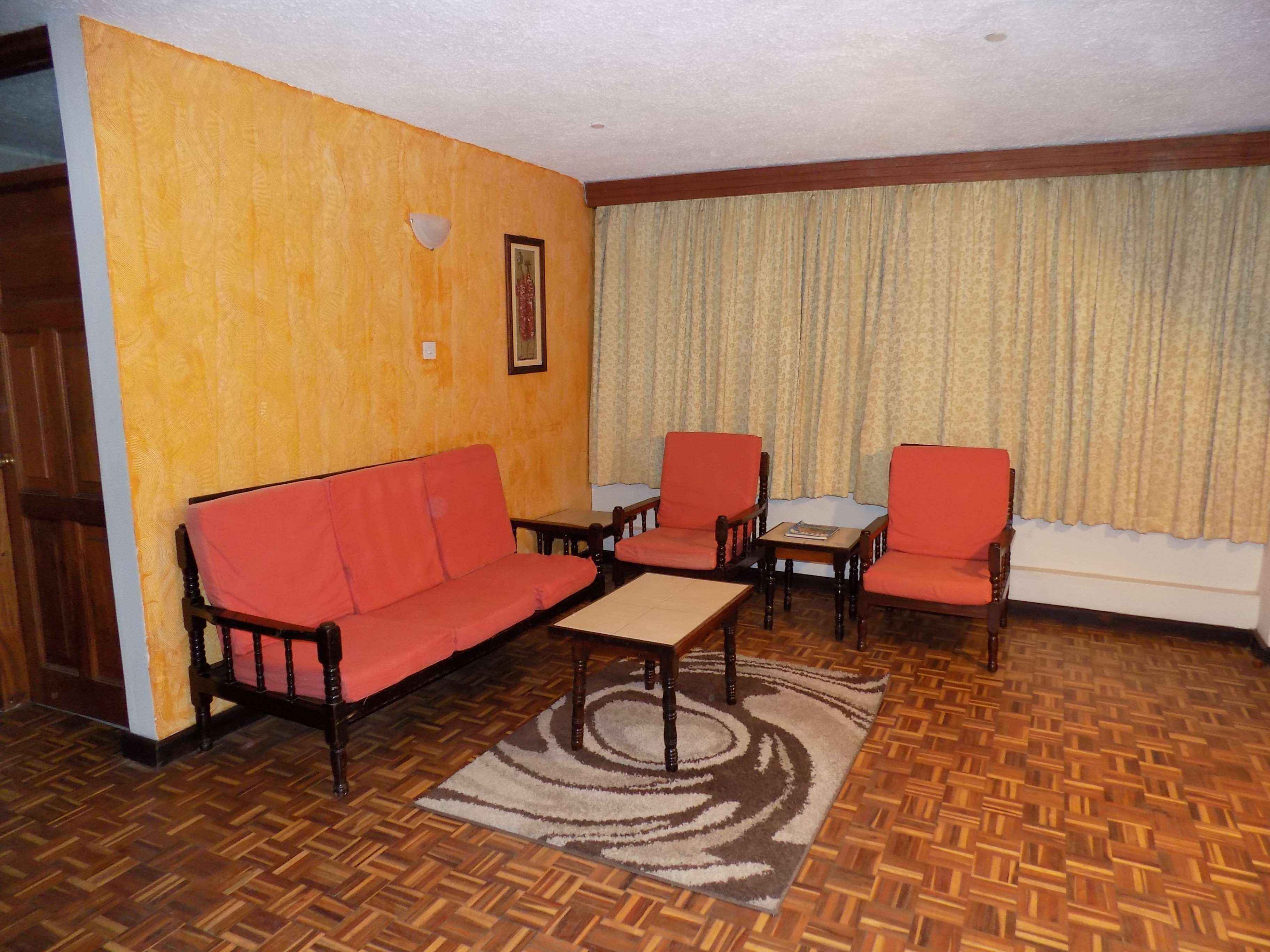 Una sala de estar con piso de madera, un sofá rojo, dos sillones, una mesita y un tapete estampado.
