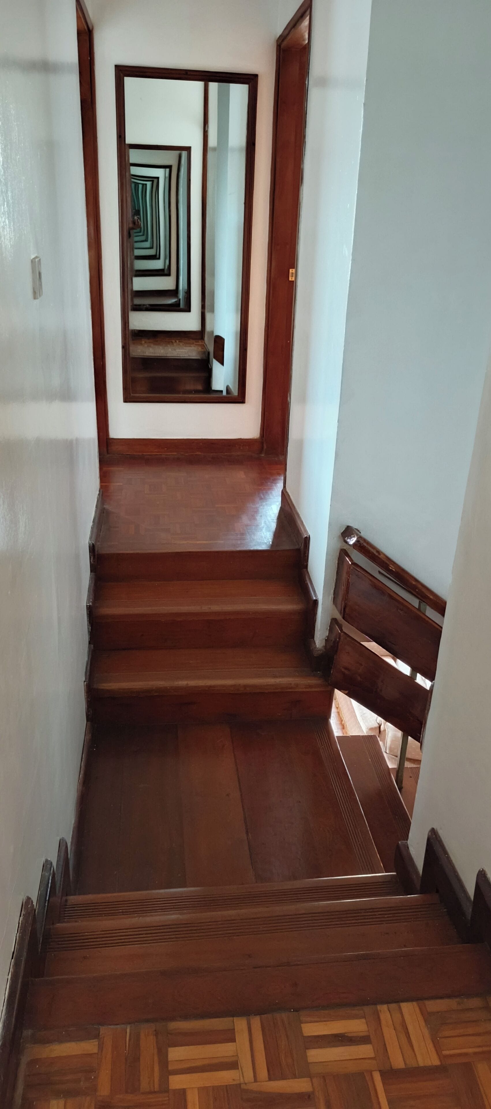 A wooden staircase with a herringbone floor pattern leading to a mirrored wall.