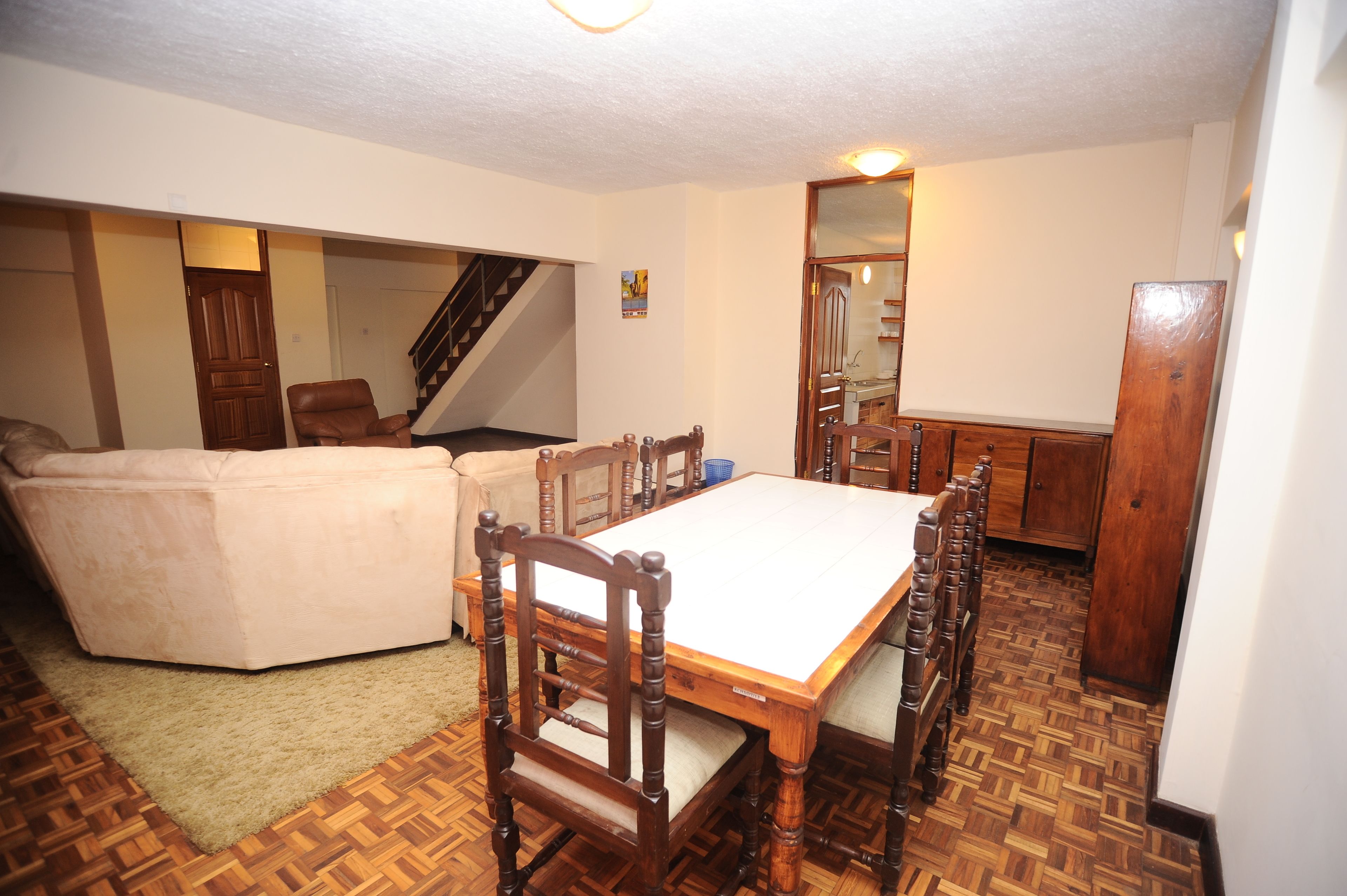 A dining area with a wooden table and chairs, a sofa, and a staircase.