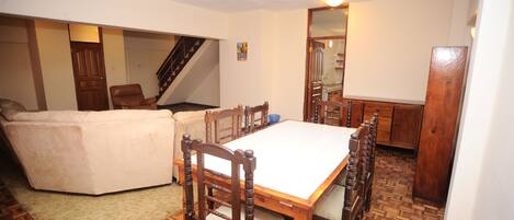 A dining area with a wooden table and chairs, a sofa, and a staircase.