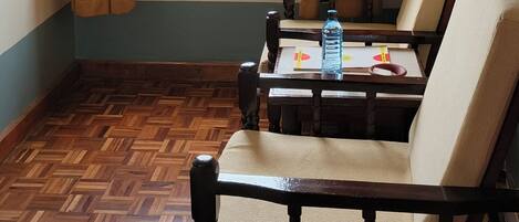 A room with a wooden herringbone floor, two wooden chairs with cushions, a window with curtains, and a view of a construction site outside.