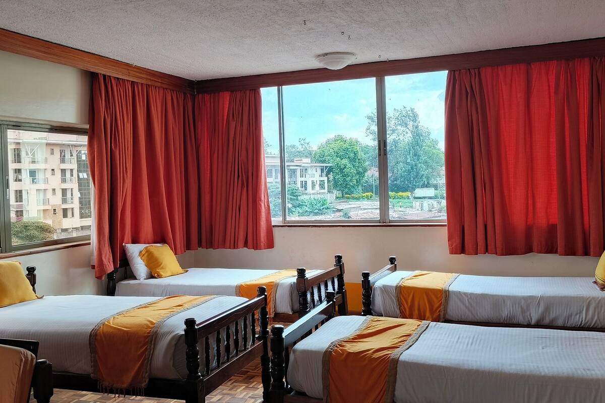Habitación de hotel con dos camas, cortinas rojas, vista a edificios y cabecera de madera.