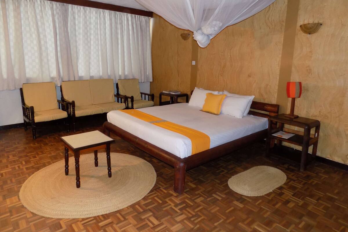 Una habitación de hotel con una cama grande, dos sillones, una mesita y una mesita de noche.
