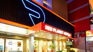 El exterior del hotel Red Planet con un llamativo letrero de neón, una tienda 7-Eleven y un cartel de taxis.