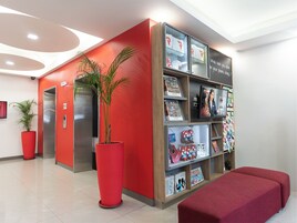 A reception area with a red wall, a large potted plant, a red bench, and a display of merchandise.