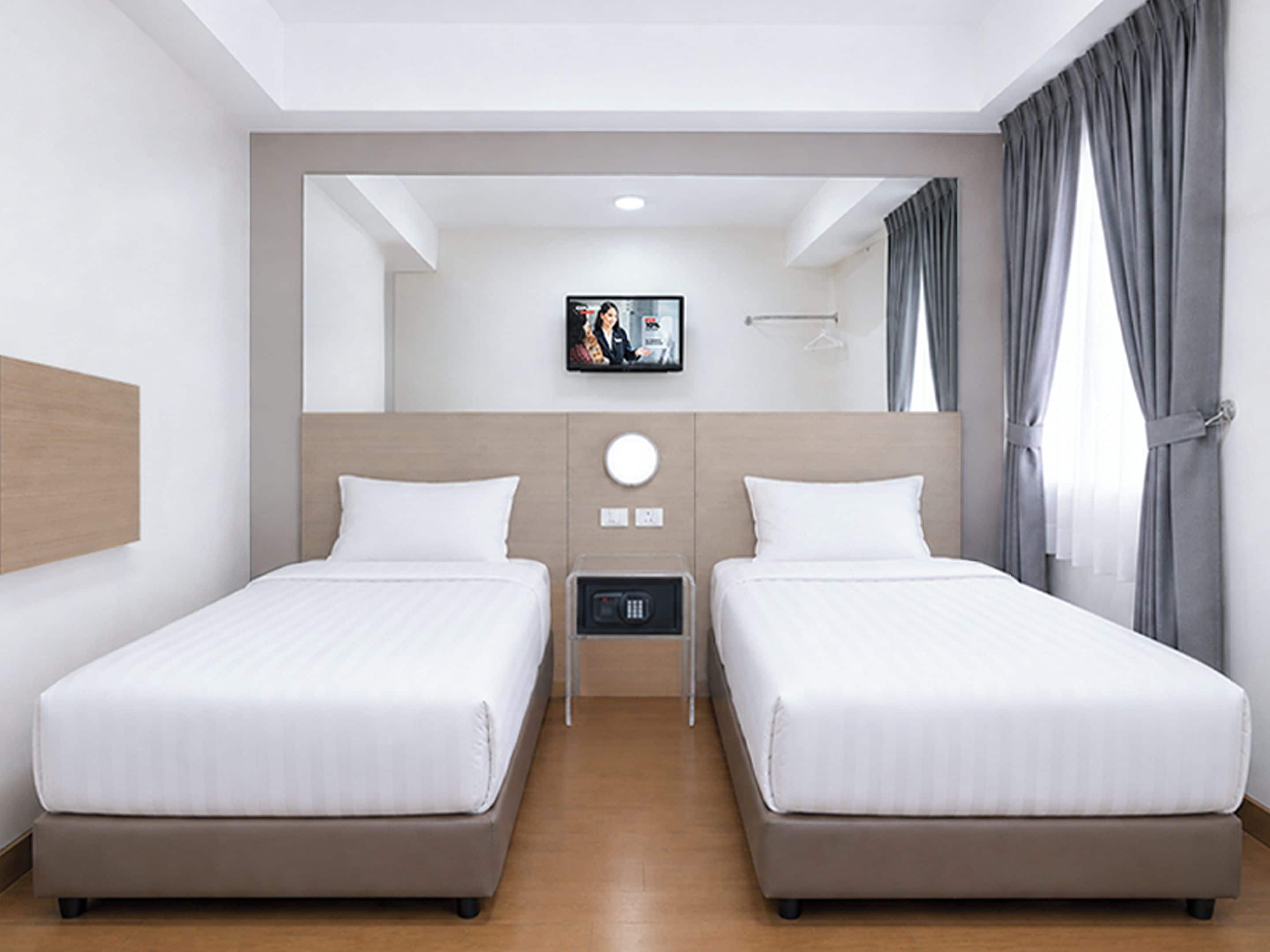 Una camera d'albergo con due letti, una televisione a parete e una finestra con tende.