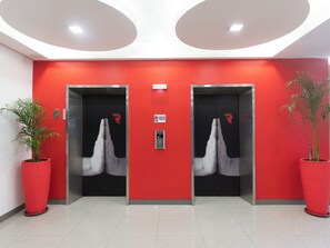 Two elevators with red walls and a CCTV sign, flanked by potted plants. - Red Planet Quezon City Timog (Quezon City)