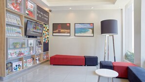 Un lobby moderno con un área de descanso en rojo y azul, un televisor de pantalla plana y un gran ventanal.