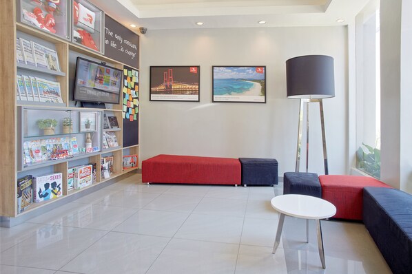 Un lobby moderno con un área de descanso en rojo y azul, un televisor de pantalla plana y un gran ventanal.