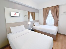 Habitación de hotel con dos camas, un televisor montado en la pared y una ventana con cortinas.