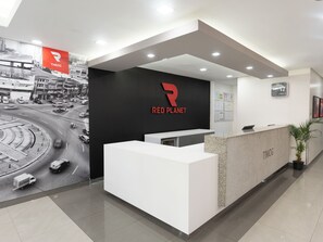 Un moderno mostrador de recepción con el logotipo 'RED PLANET', un reloj y vistas de una intersección concurrida.