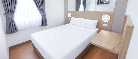 Una habitación de hotel moderna con una cama grande, una mesita de noche, un espejo y una ventana con cortinas.