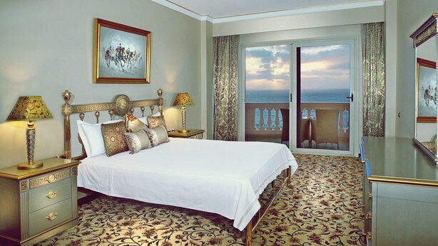 A hotel room with a large bed, a nightstand, a dresser, and a view of the ocean through a sliding door. - Tolip Alexandria (Alexandria)