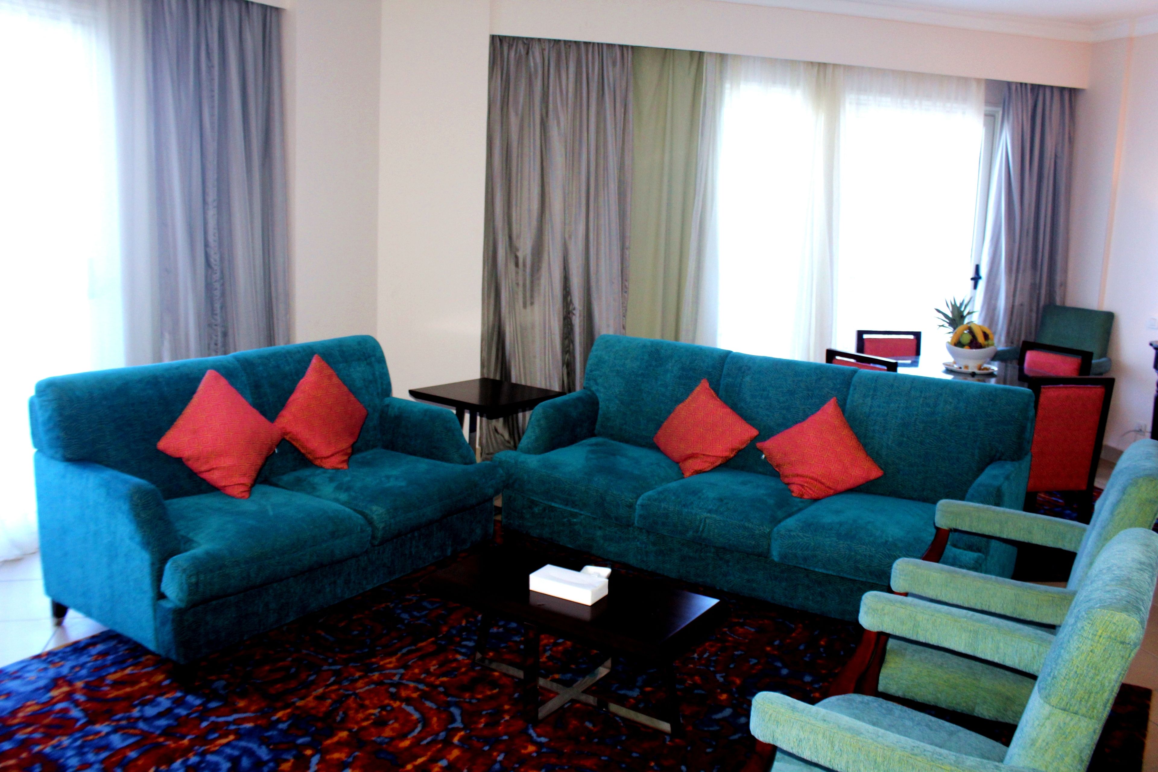 Una sala de estar con dos sofás azules, un sillón verde, una mesita y un tapete estampado.
