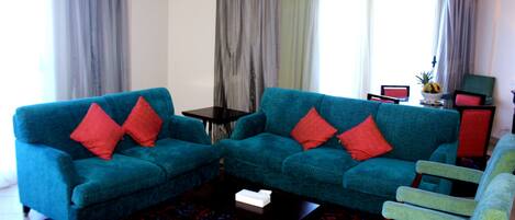 Una sala de estar con dos sofás azules, un sillón verde, una mesita y un tapete estampado.