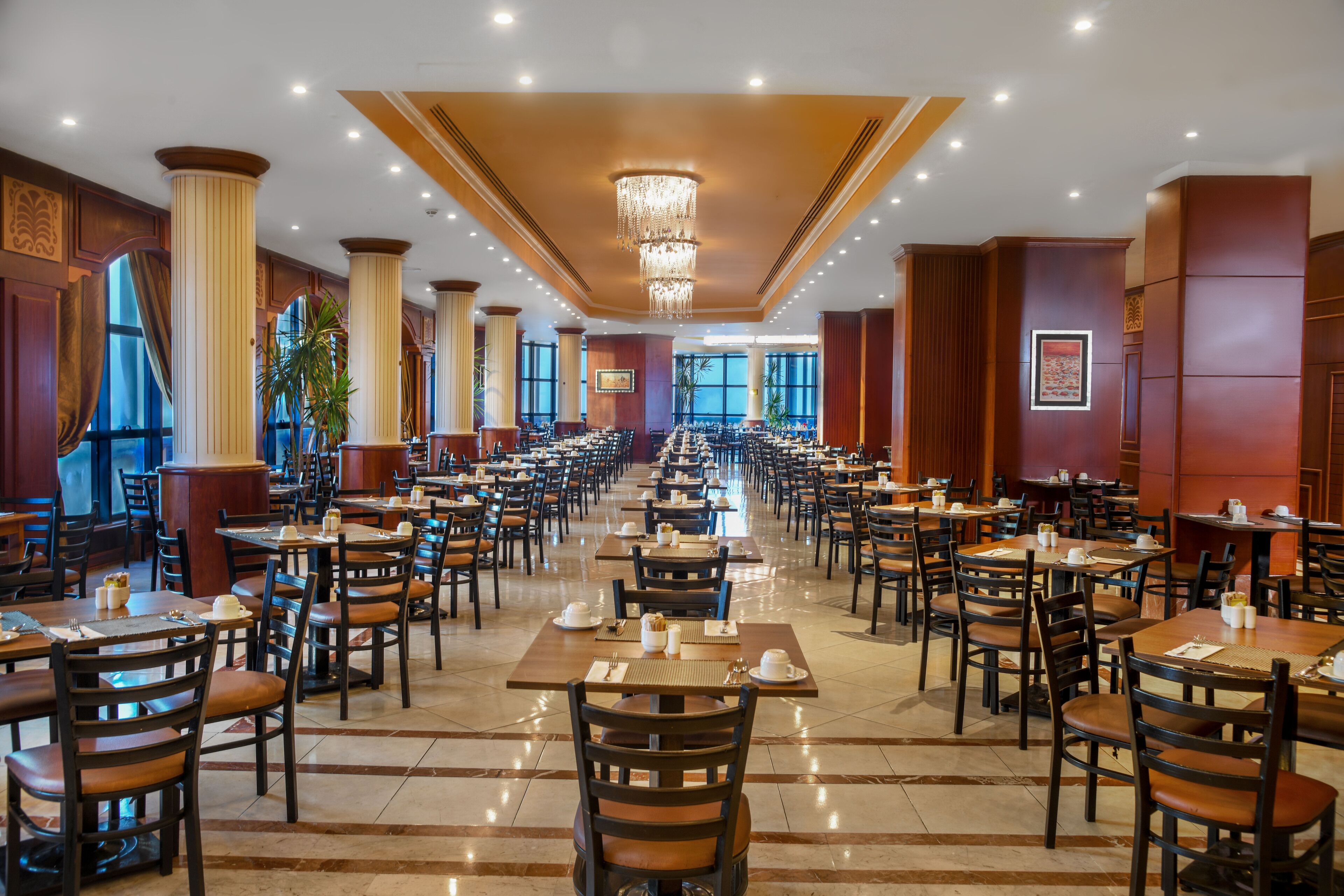 Un'ampia sala da pranzo con diversi tavoli e sedie, ampie finestre e un lampadario.