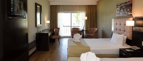 Habitación de hotel con dos camas, un escritorio, una silla, un televisor y un ventanal con cortinas.