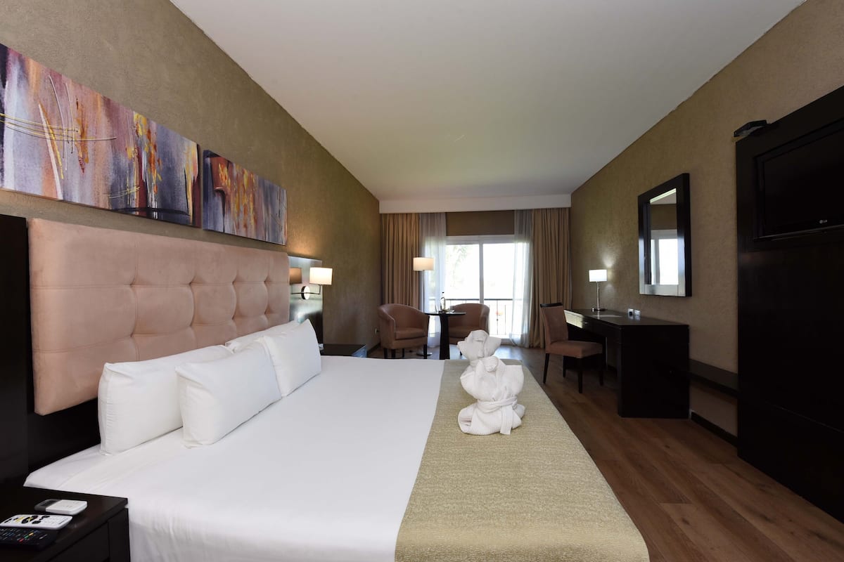 Ein Hotelzimmer mit einem großen Bett, einem Schreibtisch, zwei Stühlen, einem Fernseher und Kunstwerken an der Wand.