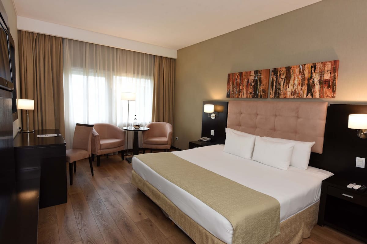 Ein Hotelzimmer mit einem großen Bett, einem Schreibtisch, einem Stuhl, einem kleinen Tisch und einem Gemälde an der Wand.