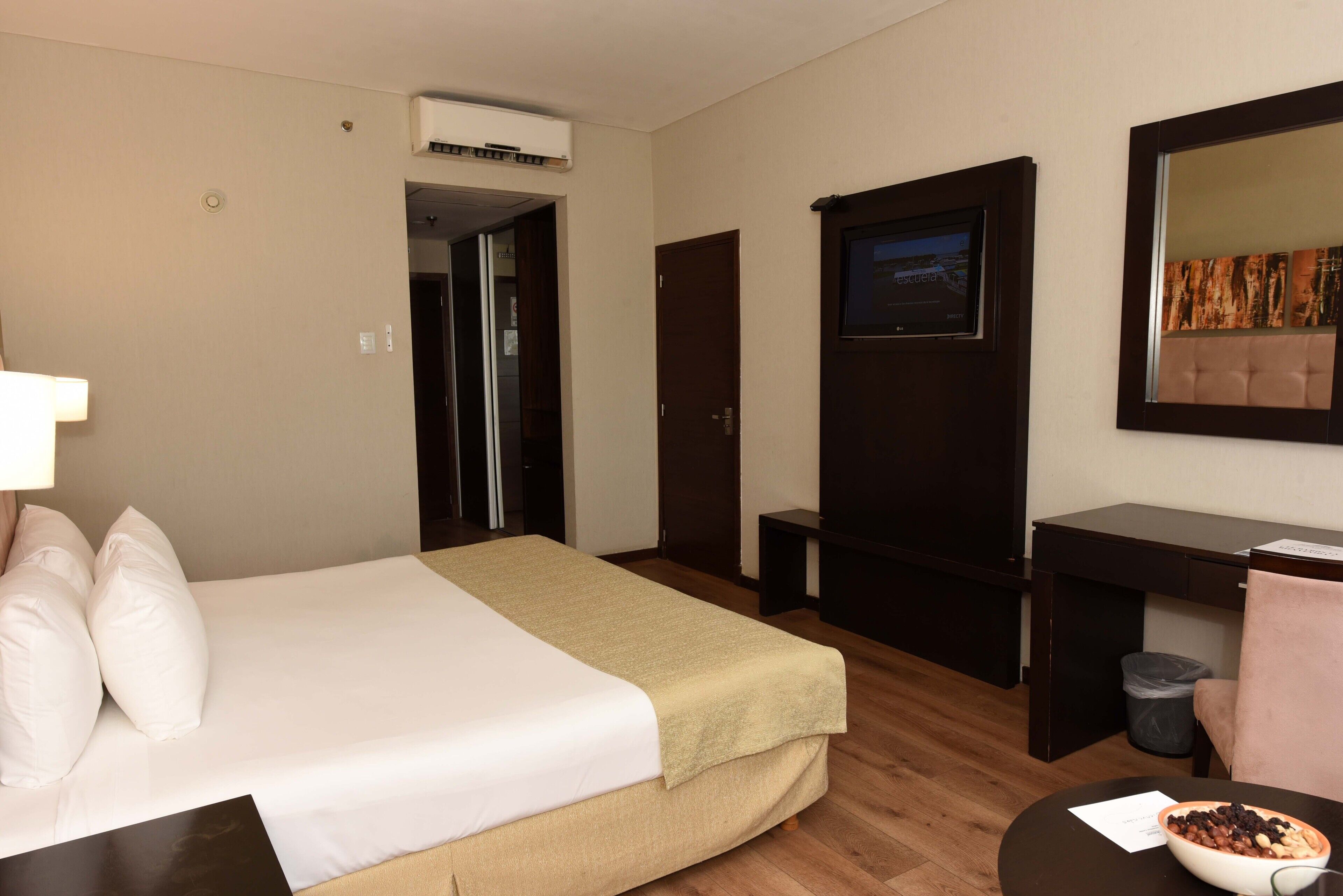 A hotel room with a bed, a desk, a chair, a TV, and a mirror.