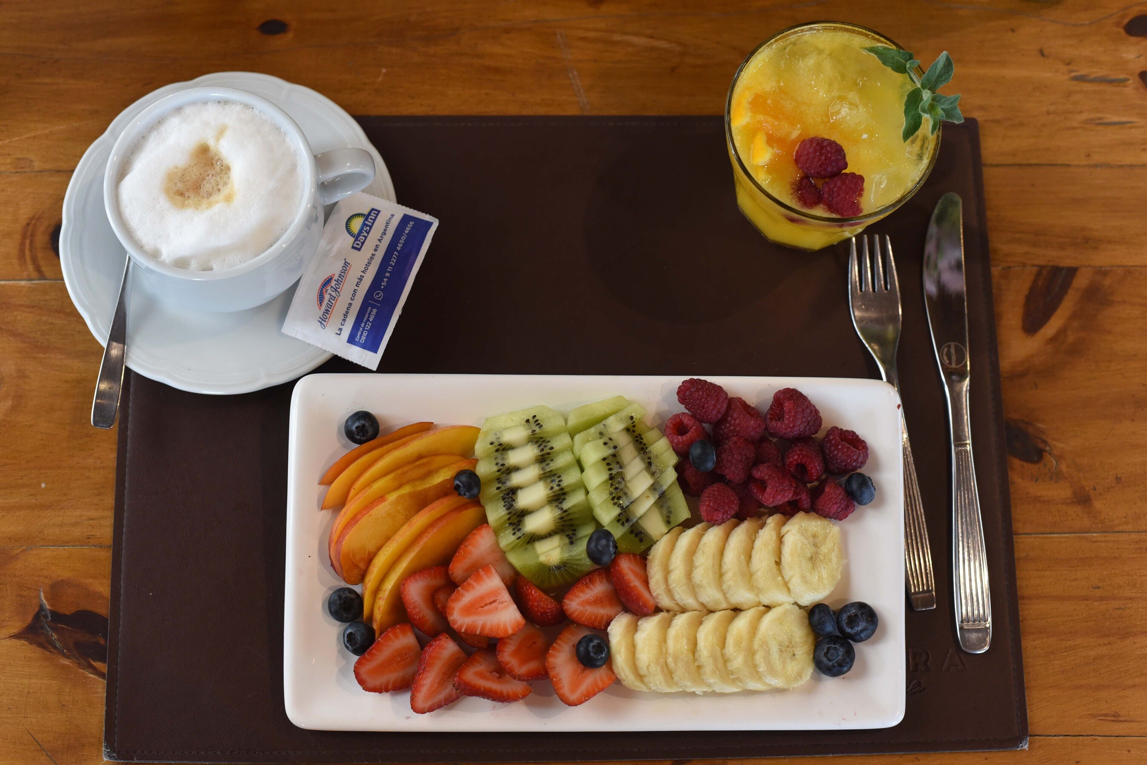 A breakfast tray with a cup of coffee, a fruit platter, and a glass of juice.