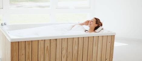 A wooden bathtub in a bright room with large windows.