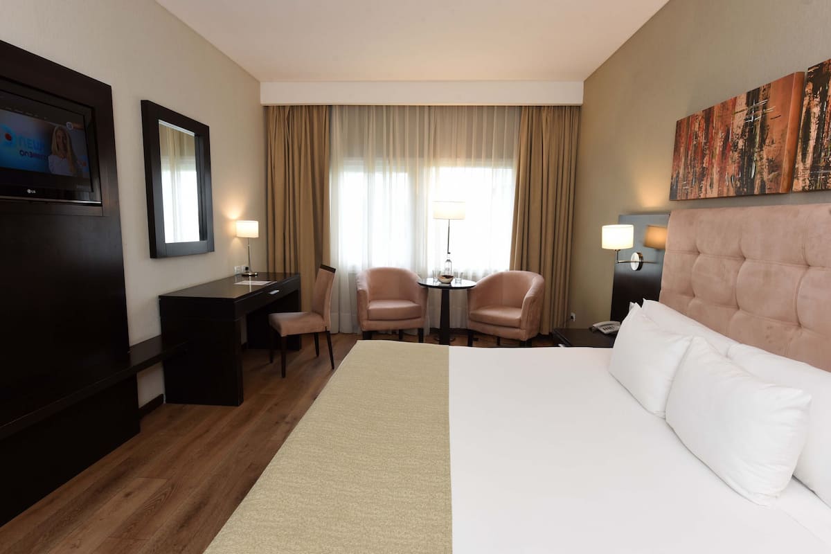 Ein Hotelzimmer mit einem großen Bett, zwei Sesseln, einem Schreibtisch und einem Fernseher.