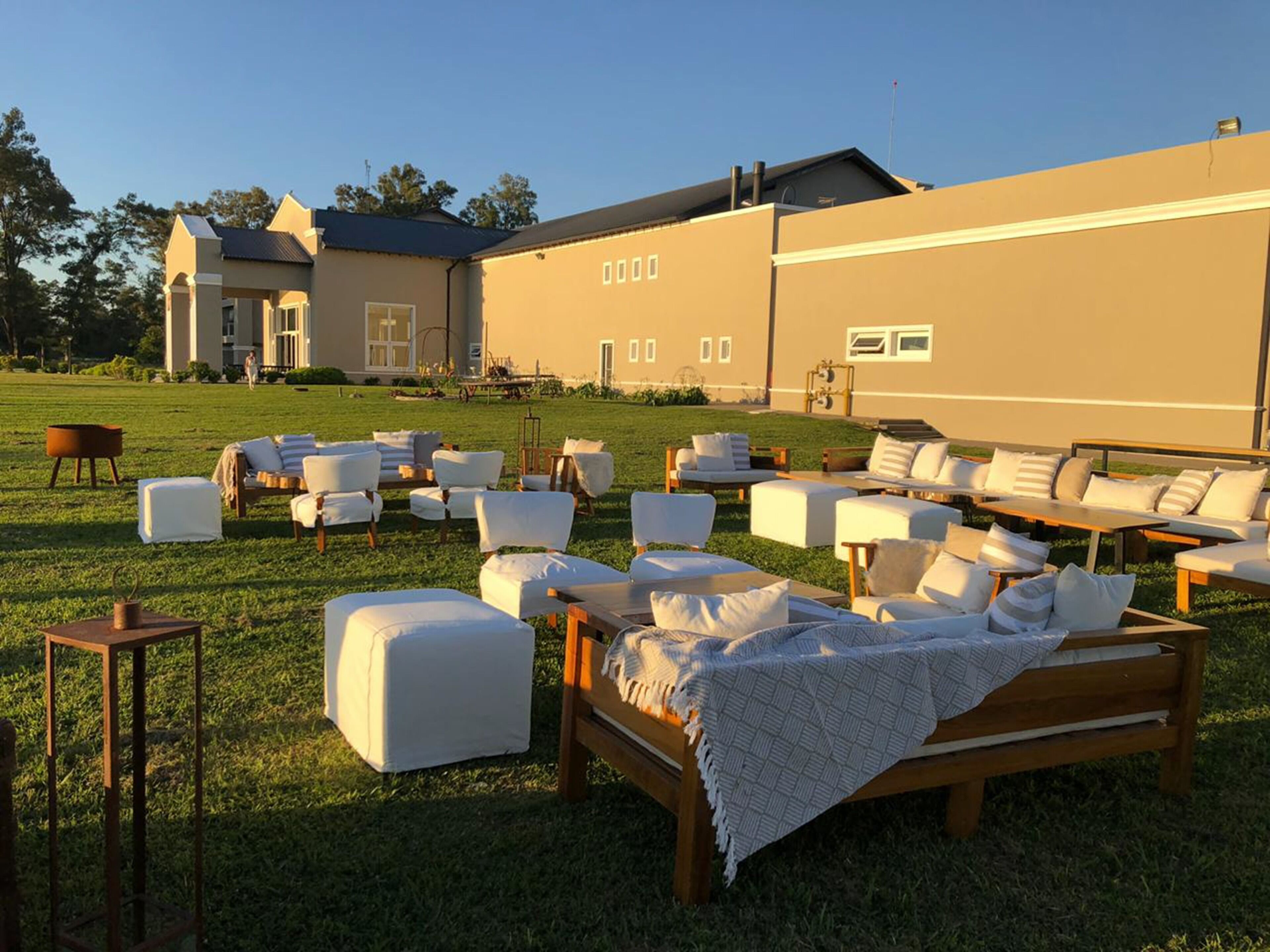 Un espace extérieur aménagé avec plusieurs fauteuils et canapés confortables, disposés sur une pelouse verdoyante, avec un bâtiment en arrière-plan.