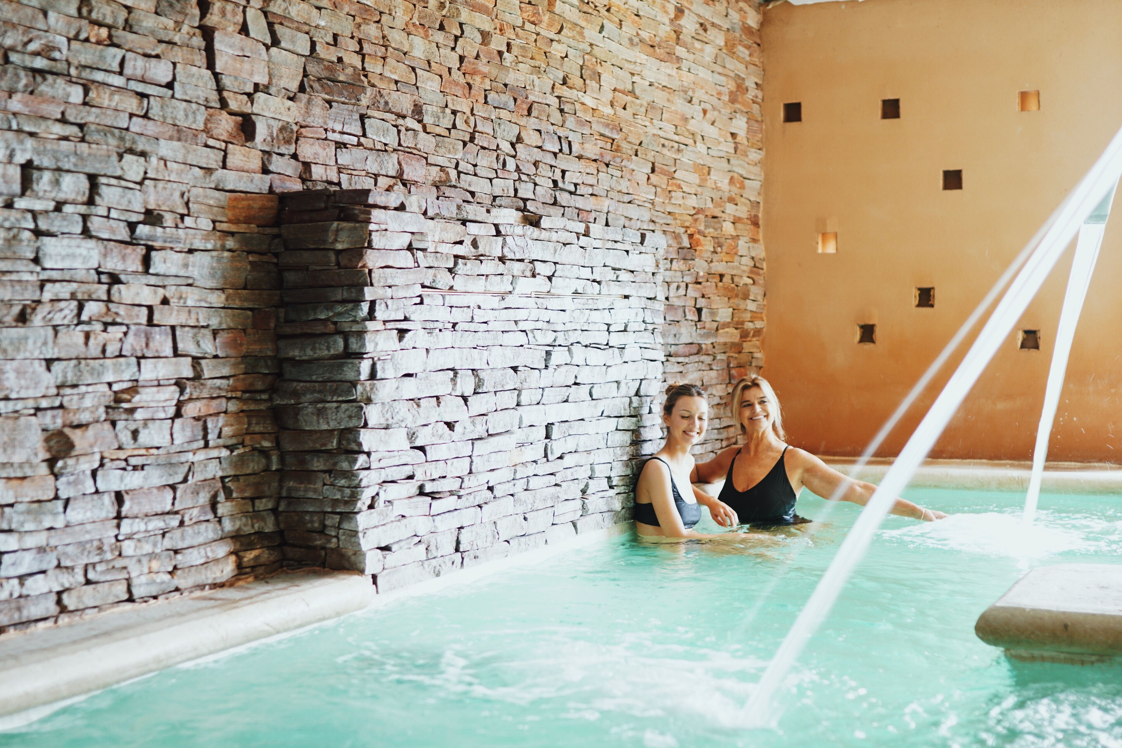 A spa pool with stone walls and a clear blue water feature.