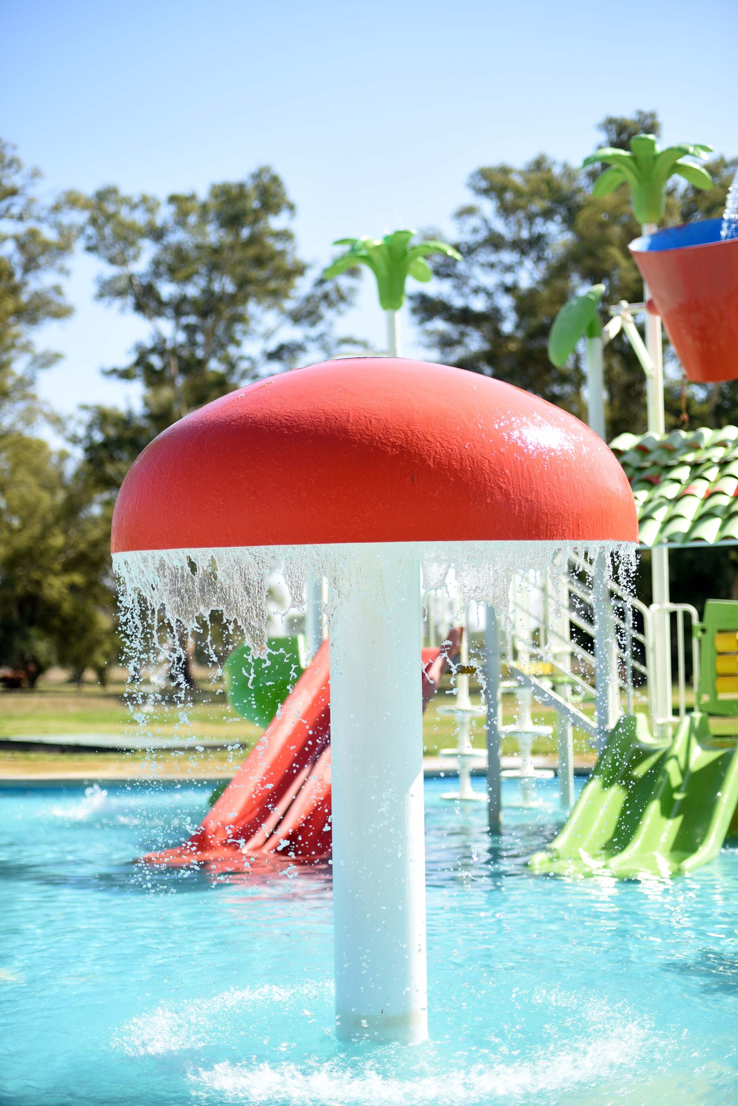 Un espace de jeux aquatiques avec une fontaine aux couleurs rouge et blanche, des toboggans et une piscine.