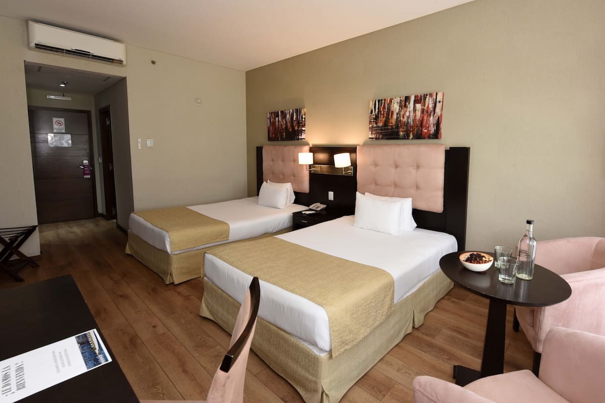 Ein Hotelzimmer mit zwei Betten, einem kleinen Tisch, einem Stuhl und einem Schreibtisch.
