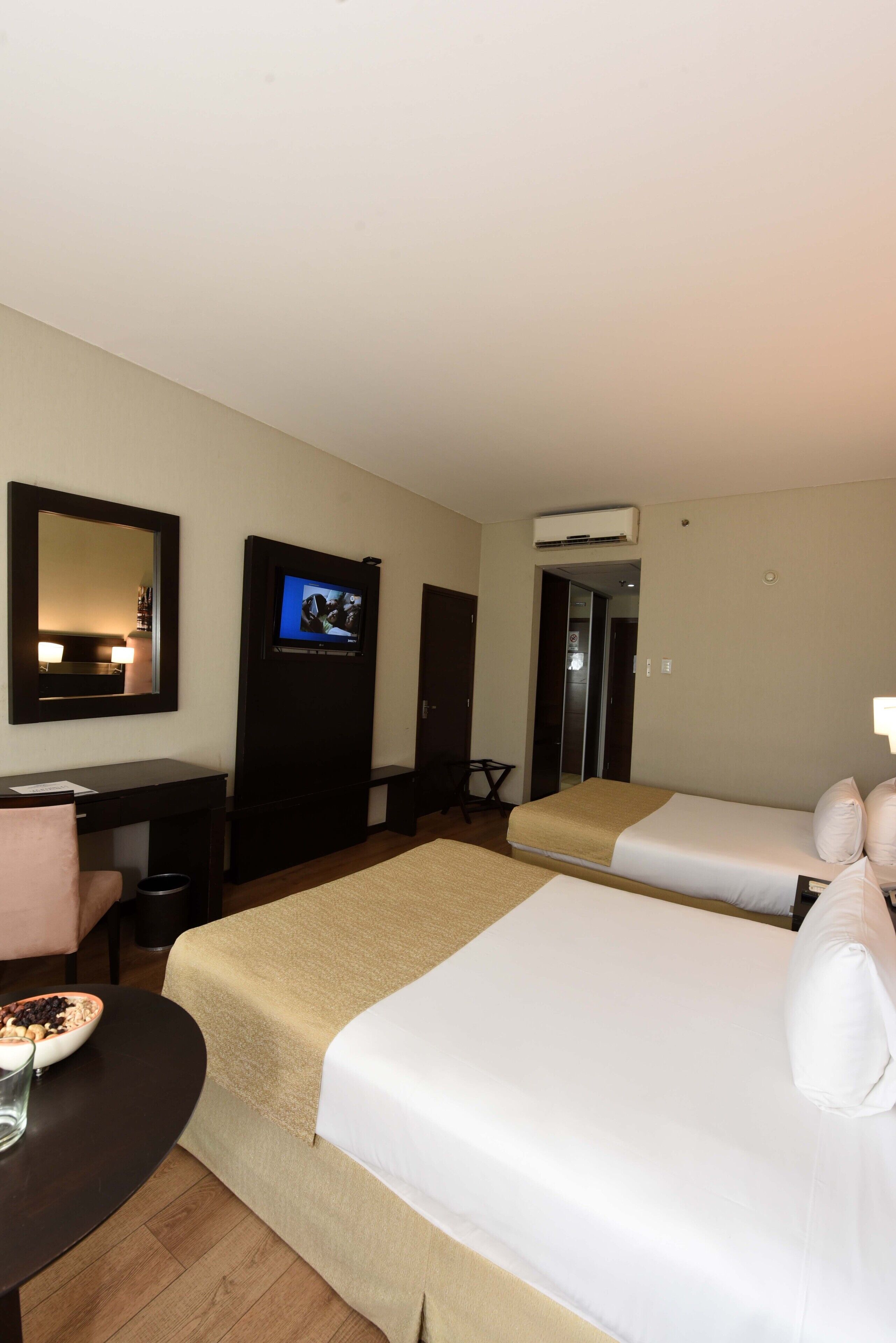 Una habitación de hotel con dos camas, un escritorio con silla, un televisor y un espejo.