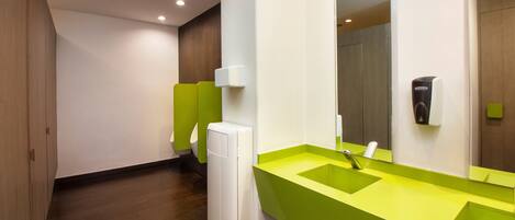 Un baño moderno con un lavamanos verde, un espejo y un secador de manos.