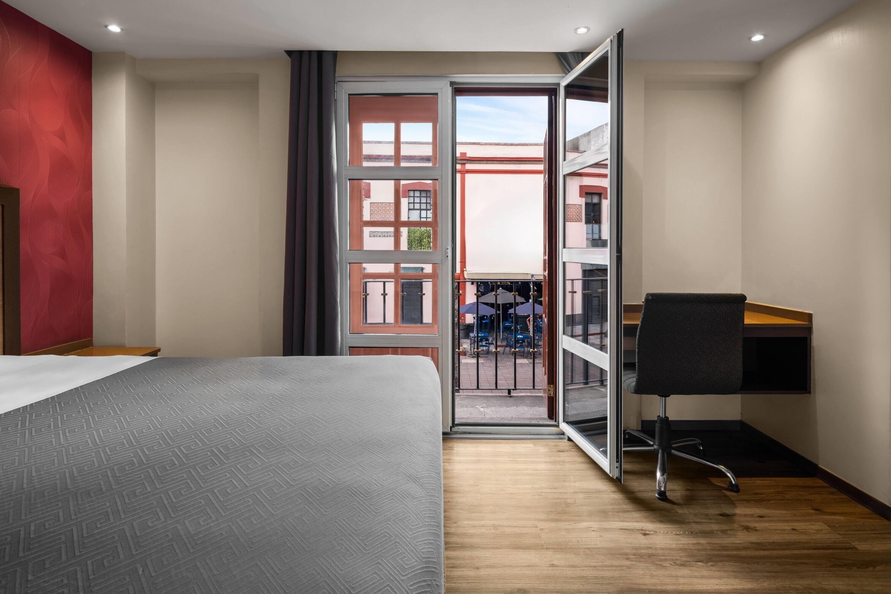 Une chambre d’hôtel avec un lit, un bureau et une vue sur le balcon extérieur.