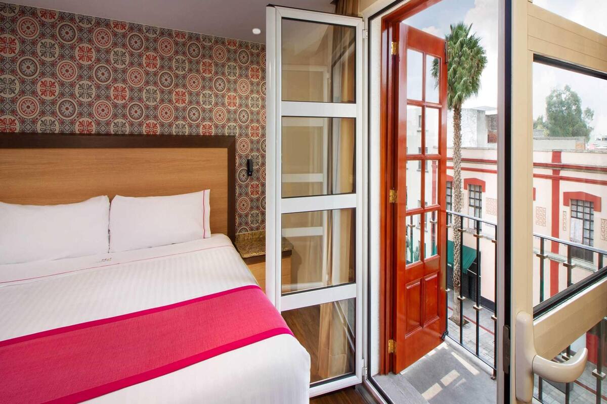 A hotel room with a bed, a large window, and a balcony.