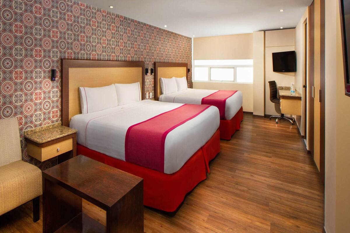 A hotel room with two beds, a wooden floor, a TV, and a desk.