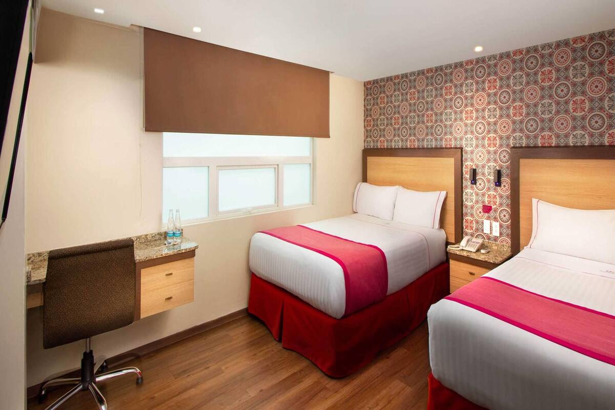 A hotel room with two beds, a desk, and a window.