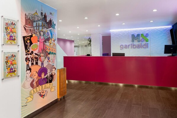 Un área de recepción con un mostrador rojo, una pared con ilustraciones coloridas y un letrero que dice 'MX garibaldi'.