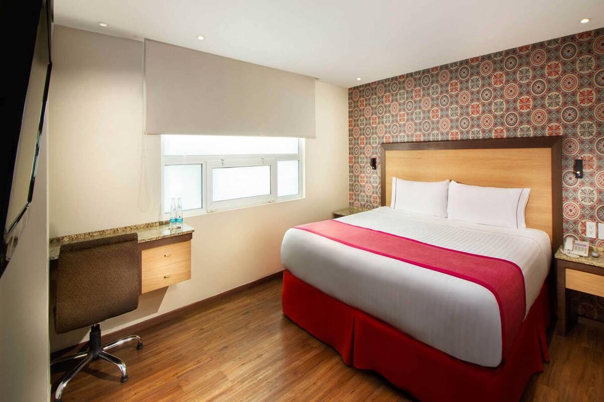 A hotel room with a bed, a desk, and a window.