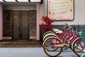 A hotel entrance with a sign in a foreign language, a flower arrangement, and a row of pink bicycles. - Hotel MX garibaldi CDMX, Trademark Collection by Wyndham (Mexico City)