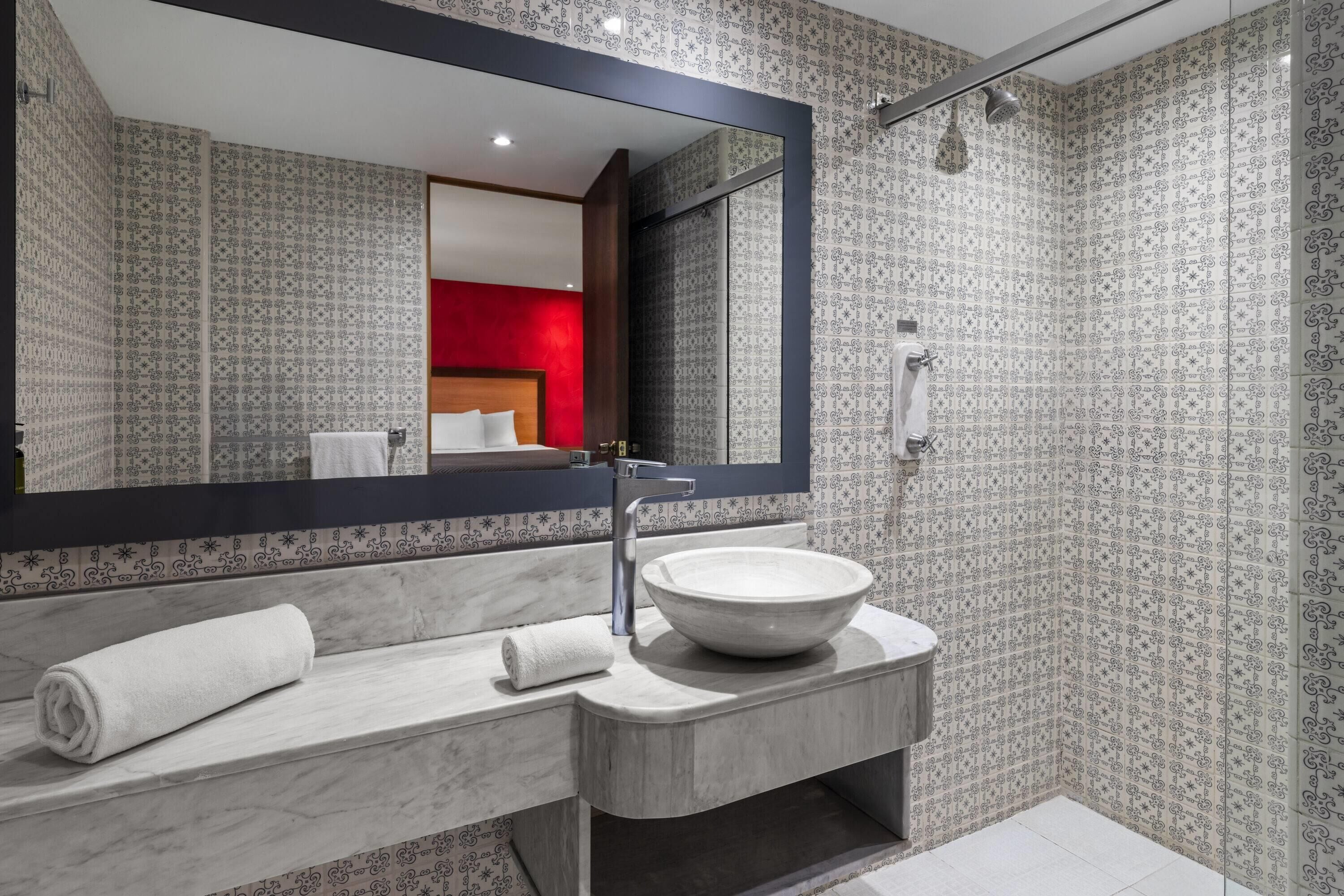 A modern bathroom with a large mirror, a marble sink, and a shower.