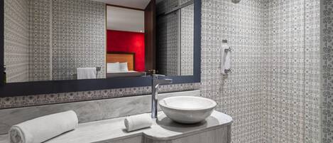 A modern bathroom with a large mirror, a marble sink, and a shower.