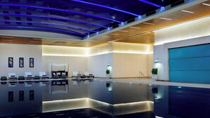 Et moderne poolområde indendørs med et spejlende gulv, liggestole og en reception.