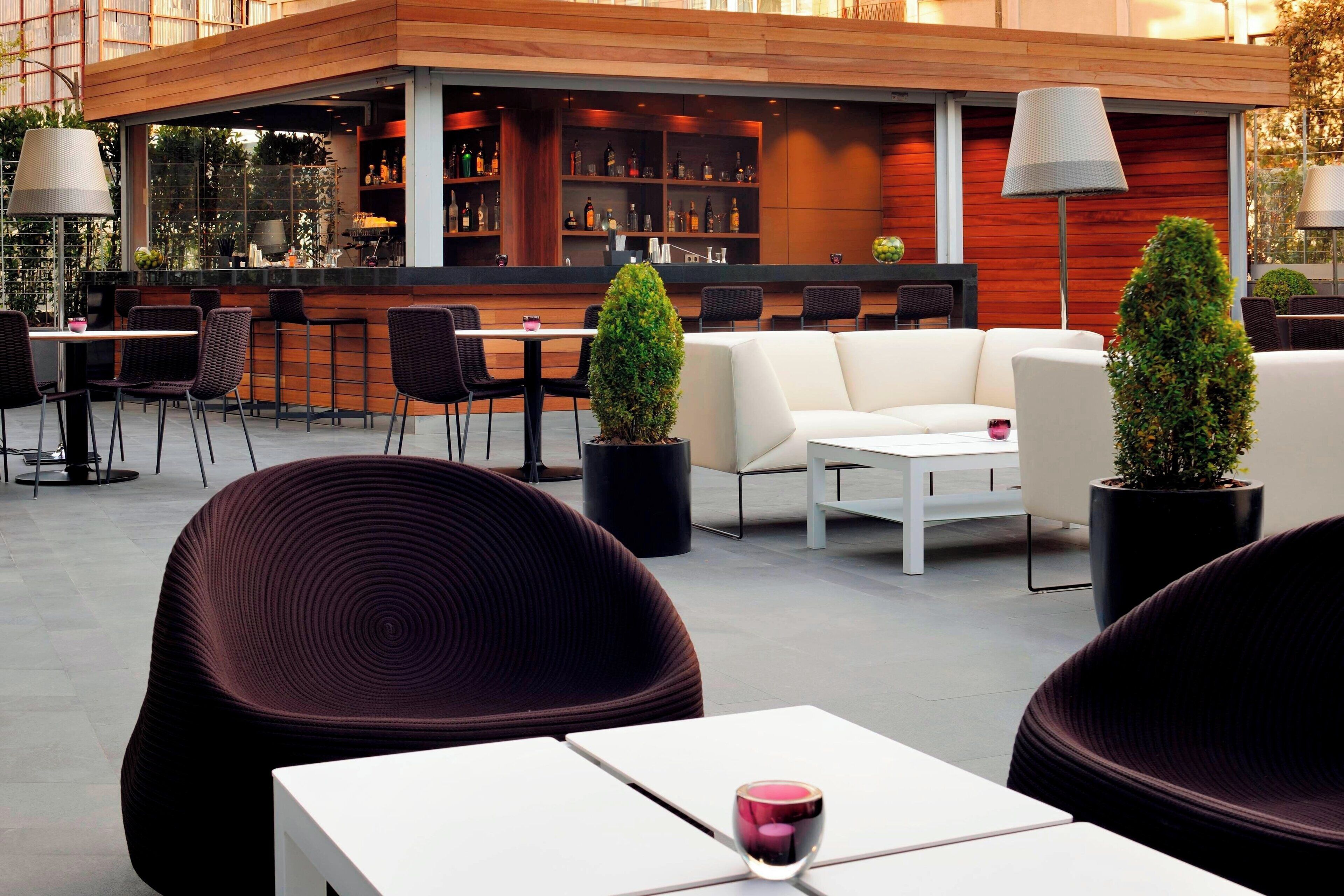 An outdoor seating area with modern furniture, a bar with shelves of bottles, and potted plants.