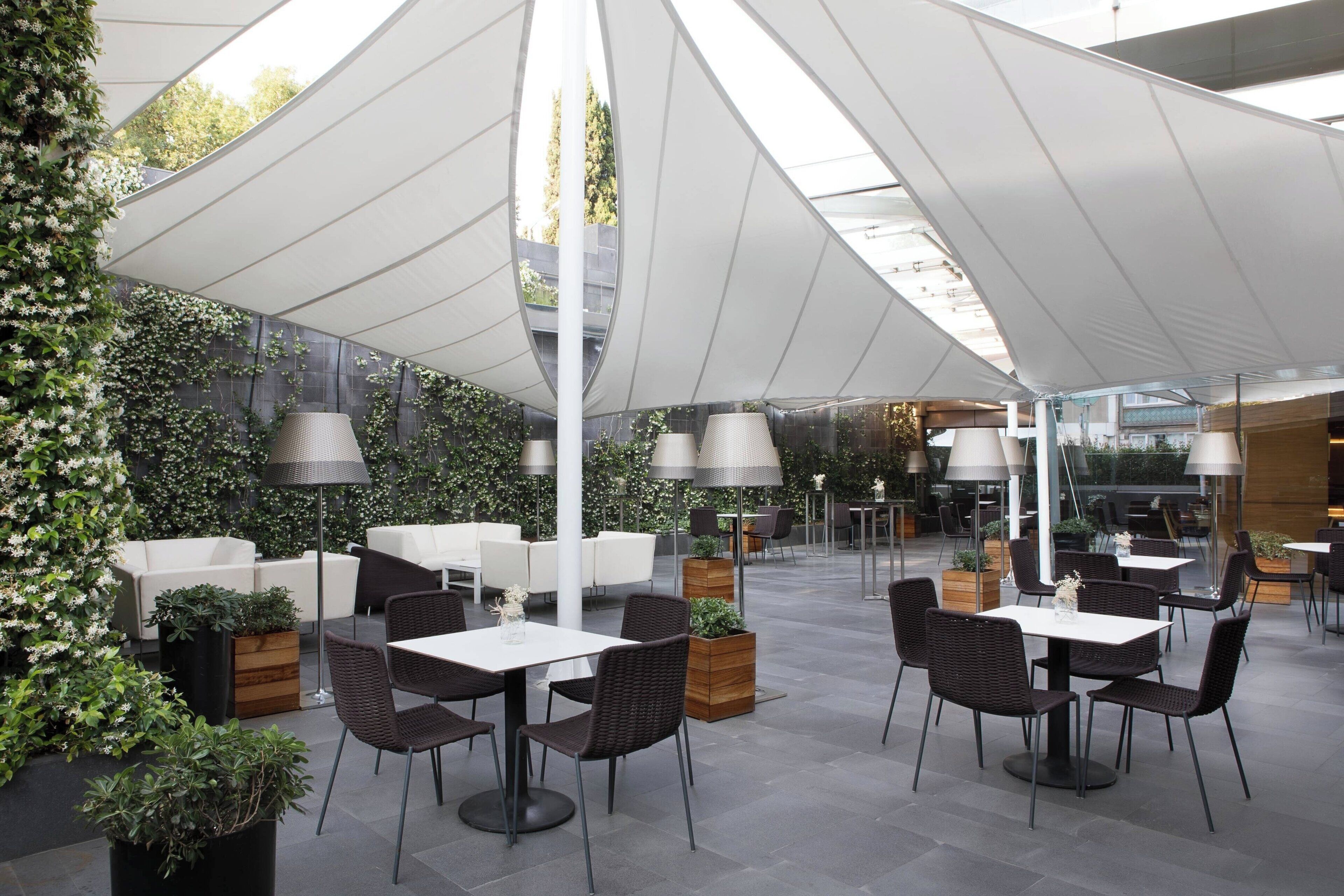 An outdoor café with tables and chairs, surrounded by greenery and white canopies.